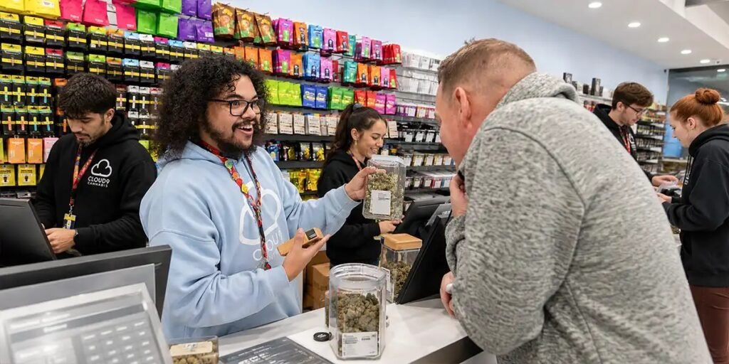 Budtender assisting customer while dispensary manager reviews inventory in cannabis retail store