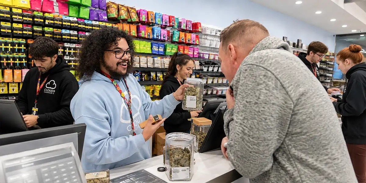 Budtender assisting customer while dispensary manager reviews inventory in cannabis retail store